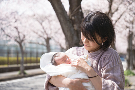 桜の木の近くで赤ちゃんを抱っこする母親