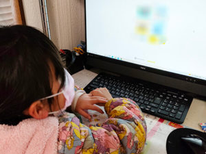 パソコン画面を見ながら、先生の英語指導を受けている小学生の女の子