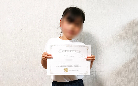 英検Jr.で好成績を収めたことを証明する賞状を手に、笑顔を見せる小学1年生の女の子