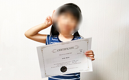英検Jr.シルバーの成績証明証を手に、ピースサインをする小学1年生の女の子
